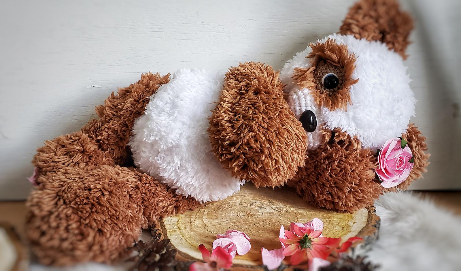 Brown and white fluffy Panda made by NTGCrochet reclining on a wood slice with pink flowers