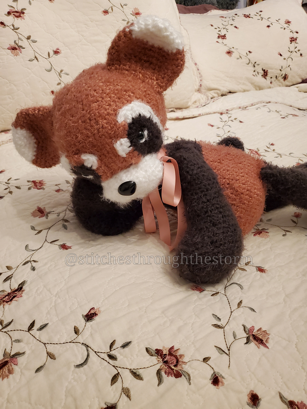 Rust, cream and charcoal fluffy Panda made by StitchesThroughTheStorm2165 reclining on a floral quilt