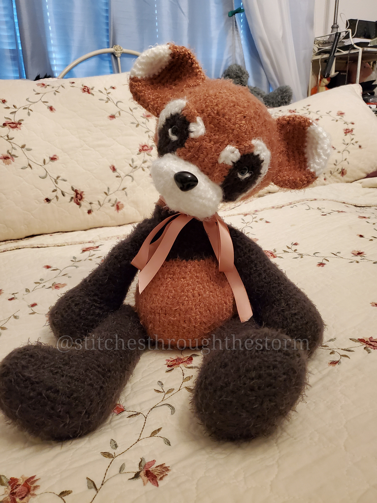 Rust, cream and charcoal fluffy Panda made by StitchesThroughTheStorm2165 sitting on a floral quilt